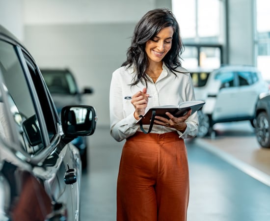 A woman with a smile as she goes through her notes symbolizing a car dealer owner's satisfaction with the performance of her car dealership.