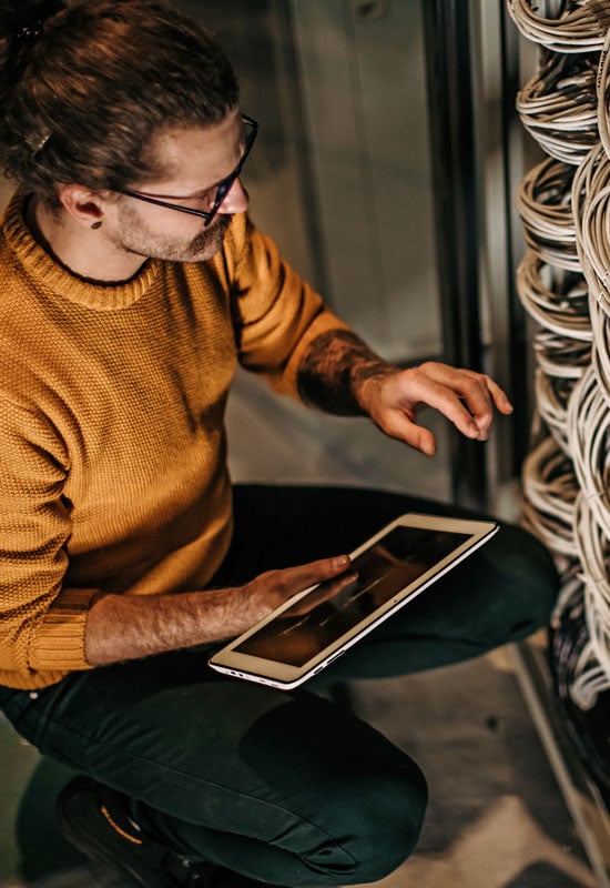 Image of an IT expert holding a tablet as he reviews a company's server for IT security gaps.