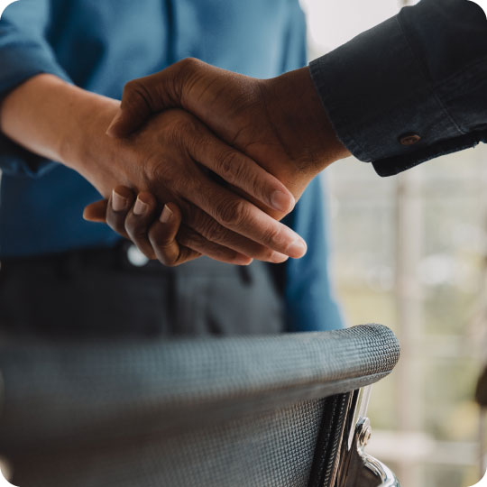 Two business men wearing bluish shirts shaking hands in partnership.